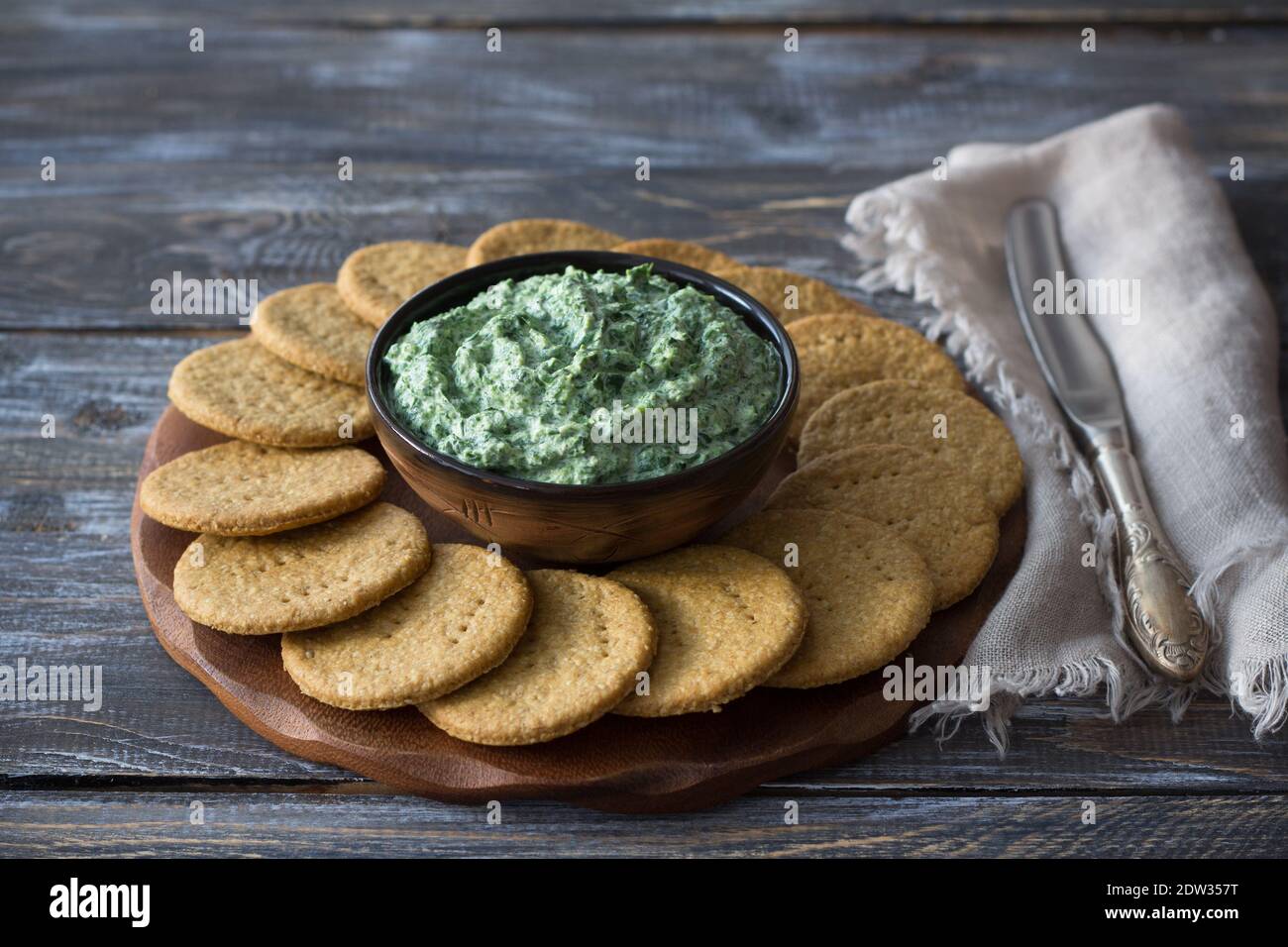 Trempez les épinards verts avec du fromage à la crème, de l'ail et des épices sur une planche en bois avec des craquelins à l'avoine, style rustique, concentration sélective. Des aliments sains faits maison Banque D'Images