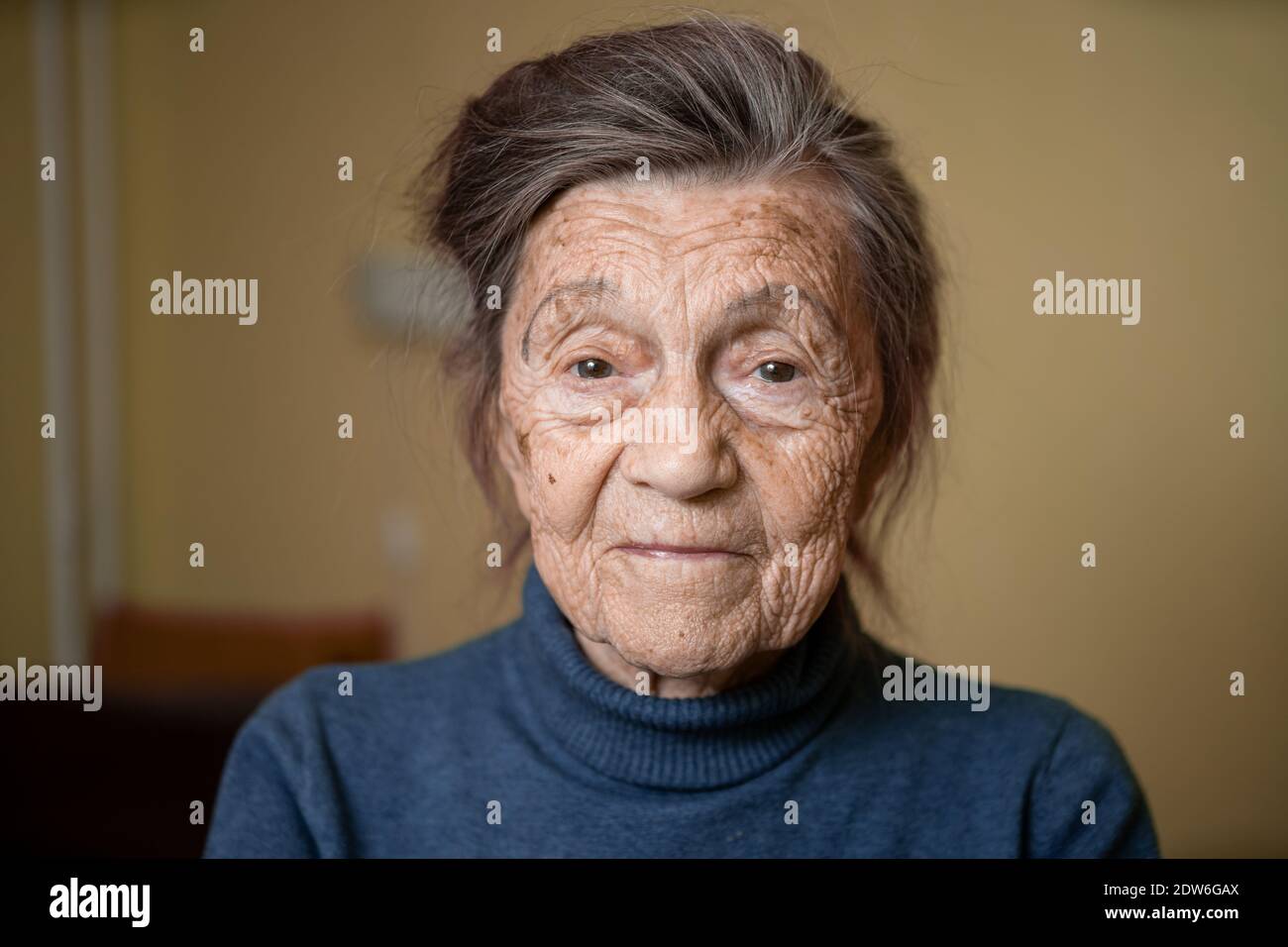 90 ans mignonne femme âgée avec cheveux gris et rides visage, portant chandail, portrait grand, souriant et regardant joyeusement, arrière-plan de la pièce. TH Banque D'Images