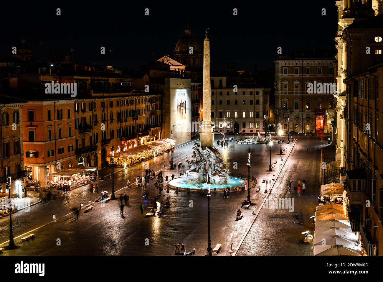 Vue sur la Piazza Navona la nuit avec des cafés illuminés et la fontaine des quatre rivières de Bernini illuminée pendant que les touristes aiment la soirée. Banque D'Images