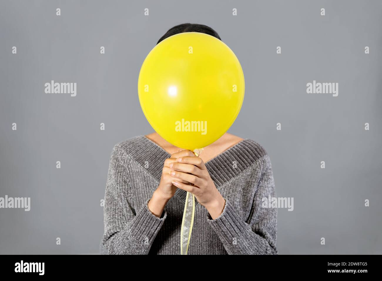 Gros plan sur une jeune femme qui cache son visage de couleur jaune ballon sur fond gris Banque D'Images