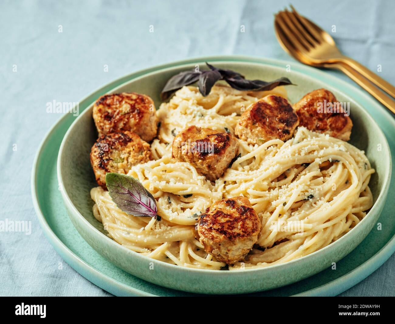 Boulettes de parmesan courgettes aux pâtes Carbonara dans une assiette verte sur une nappe bleue. Vue rapprochée de la carbonara crémeuse avec boulettes de viande de bœuf. Banque D'Images