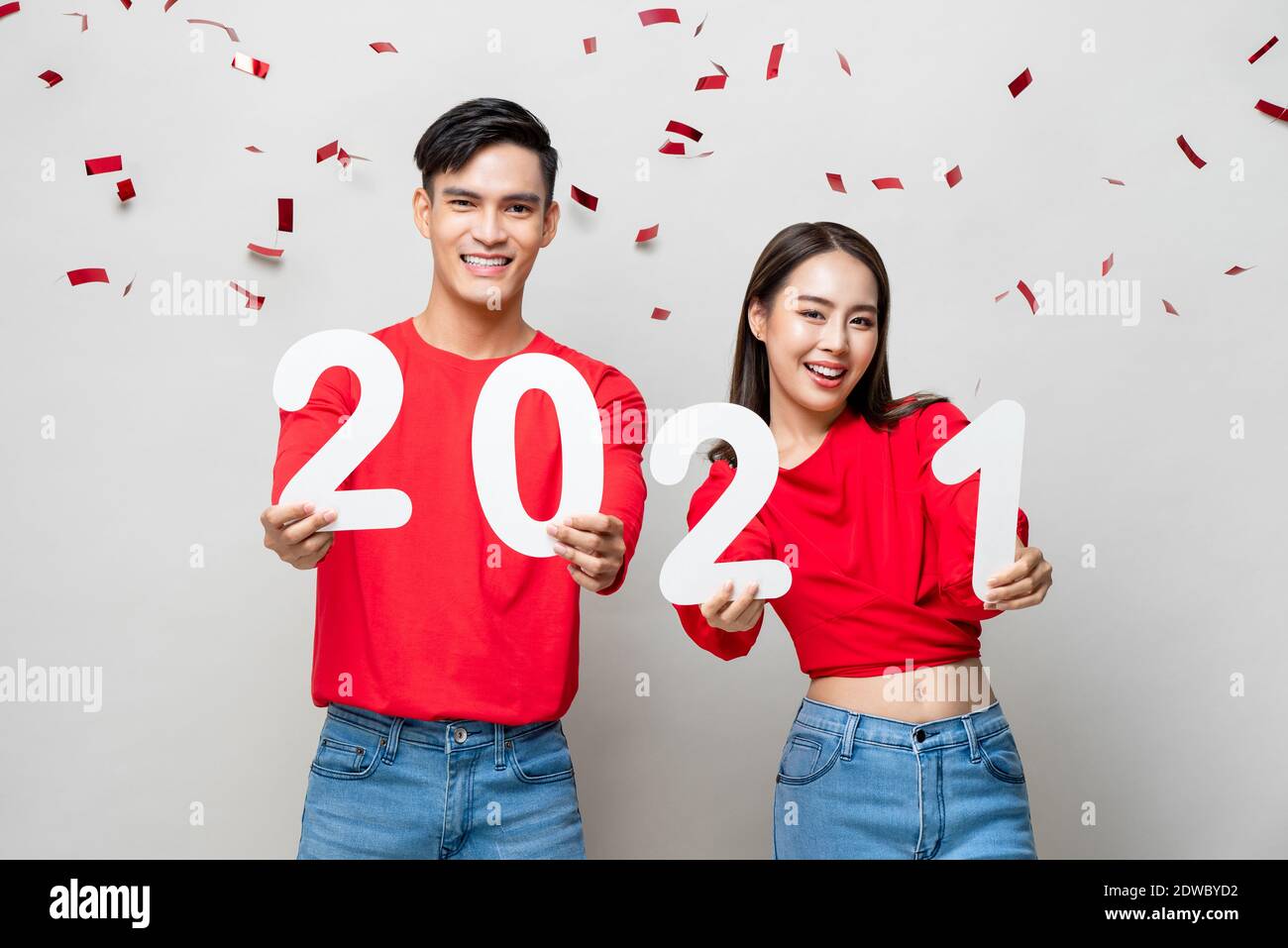 Portrait d'un couple asiatique souriant en tenue décontractée rouge 2021 numéros pour le nouveau concept de l'année en gris clair arrière-plan avec confetti Banque D'Images