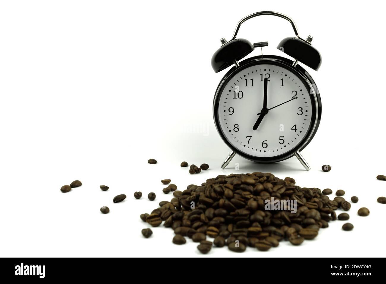 Une horloge sur une assiette blanche et des grains de café torréfiés. L'horloge pointe à sept heures le matin Banque D'Images
