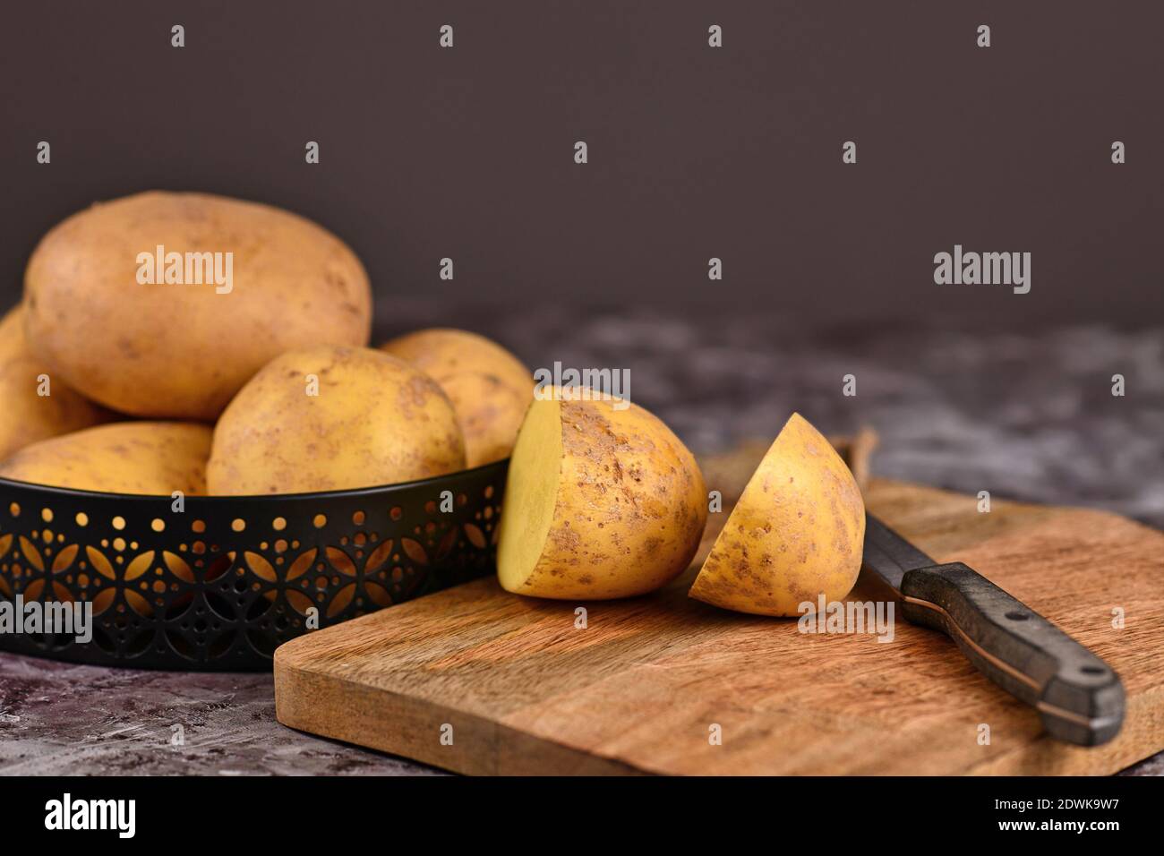 Couper la pomme de terre brute avec pelage sur la planche à découper en bois avec pile de pommes de terre entières en arrière-plan Banque D'Images
