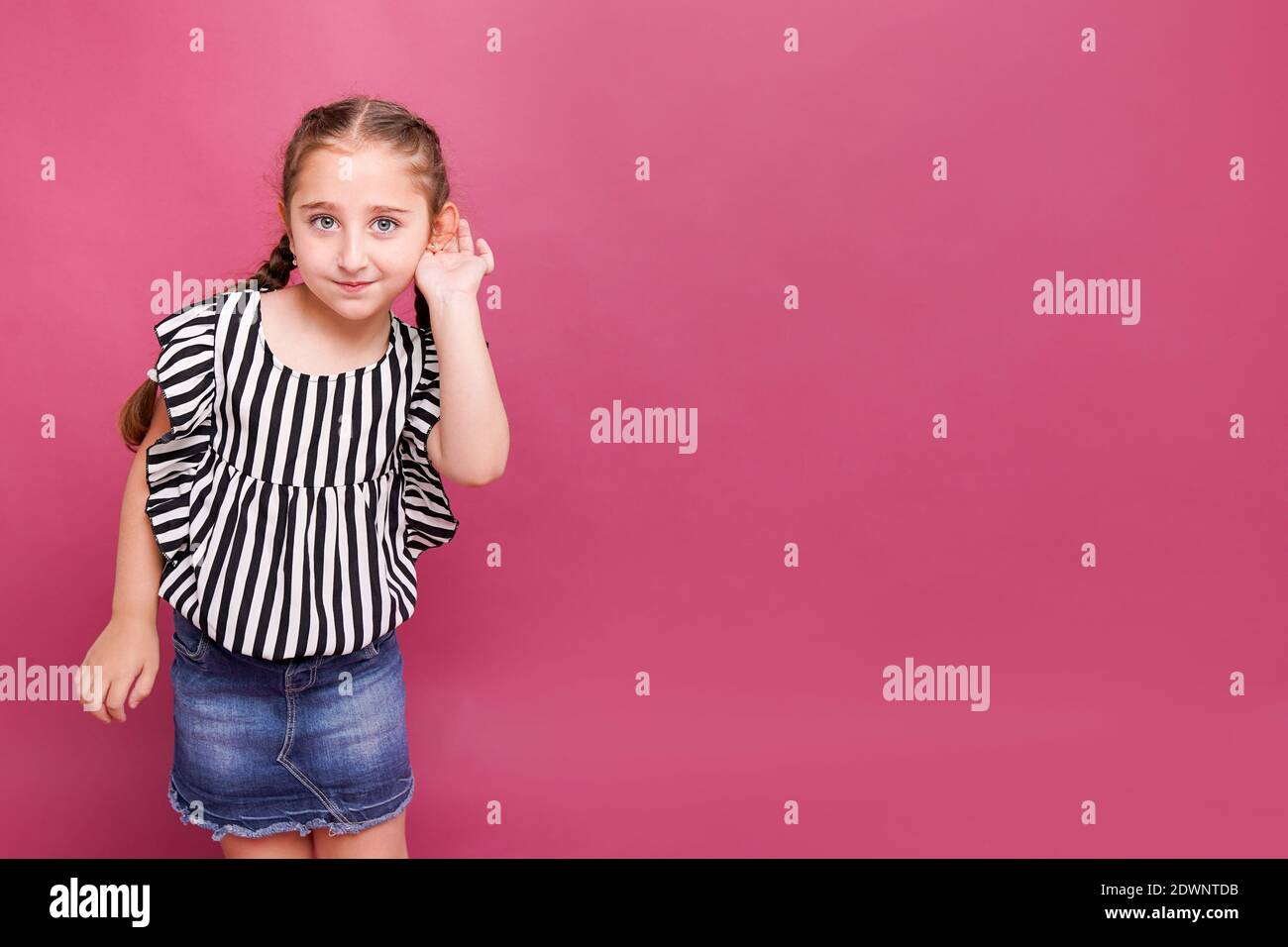 une fille de 7-8 ans tient sa main près de son oreille avec écouter quelque chose sur fond rose Banque D'Images