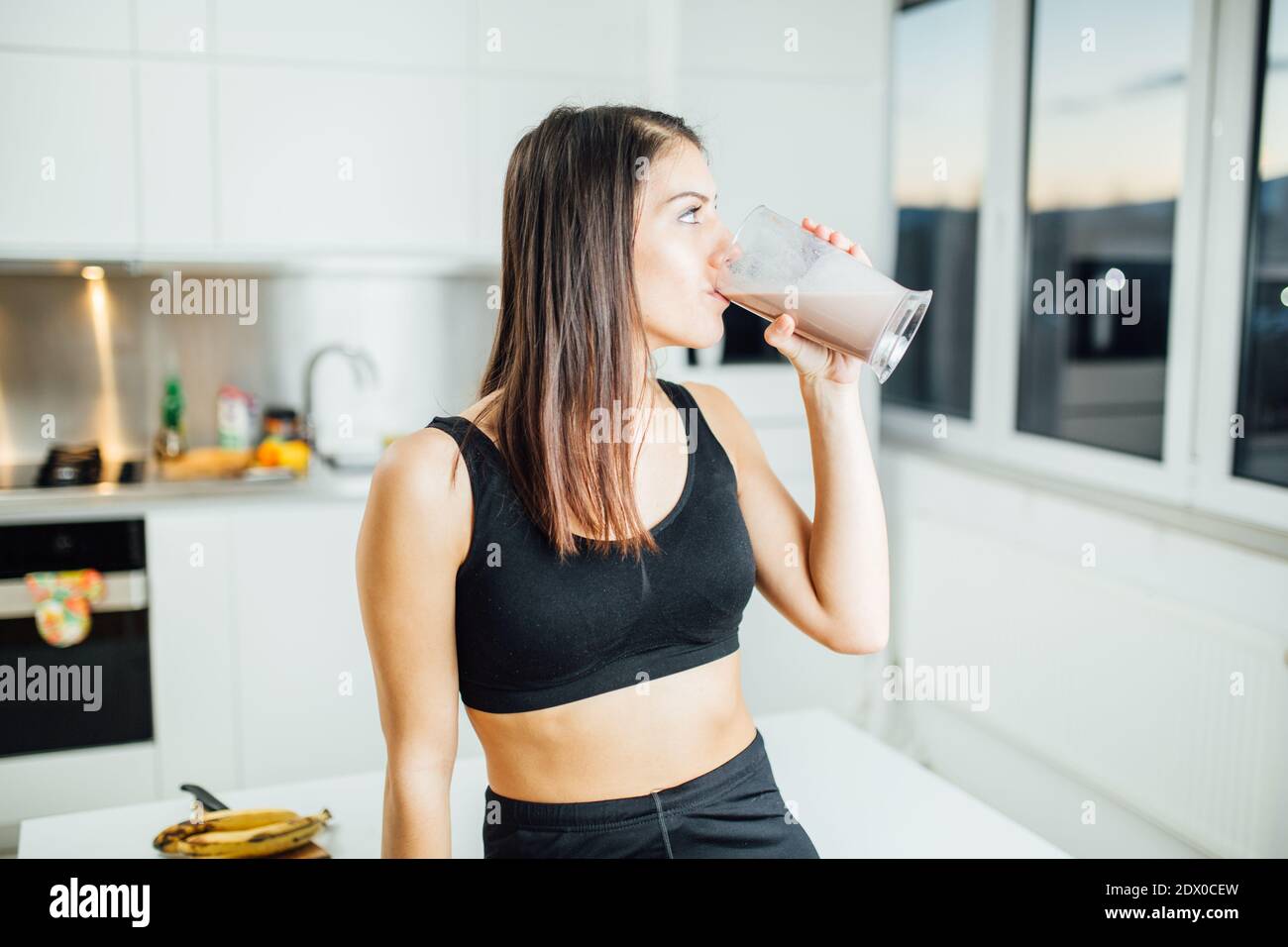 Femme en sportswear boire doux banane protéines chocolat poudre milkshake smoothie.Drinking protéines après à l'entraînement à la maison.Whey, banane et faible graisse Banque D'Images