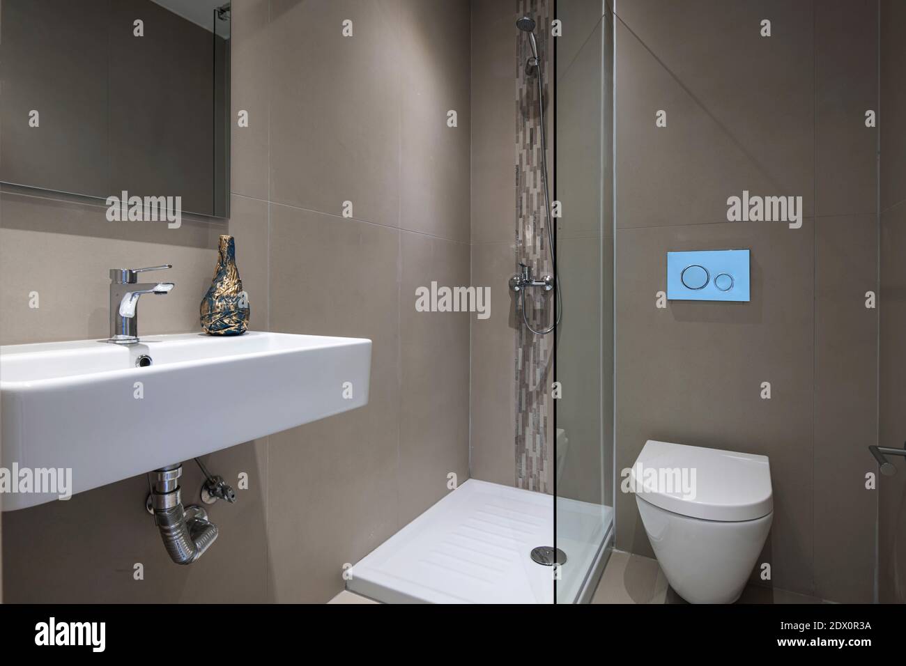 Intérieur gris moderne de la petite salle de bains avec douche en verre, miroir rectangulaire, toilettes montées, lavabo blanc suspendu Banque D'Images