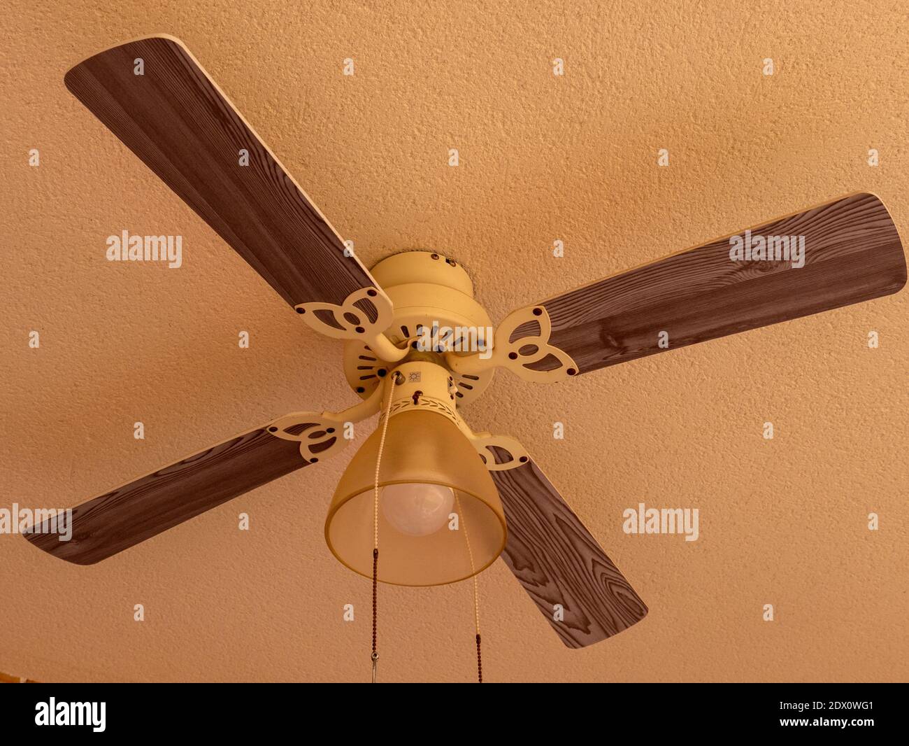 Un gros plan d'un ventilateur de plafond en bois et métal sur fond beige Banque D'Images