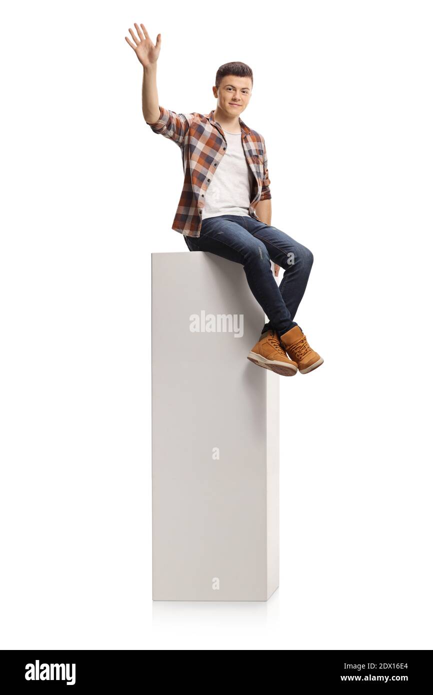 Adolescent de sexe masculin assis sur une colonne haute et agitant à caméra isolée sur fond blanc Banque D'Images
