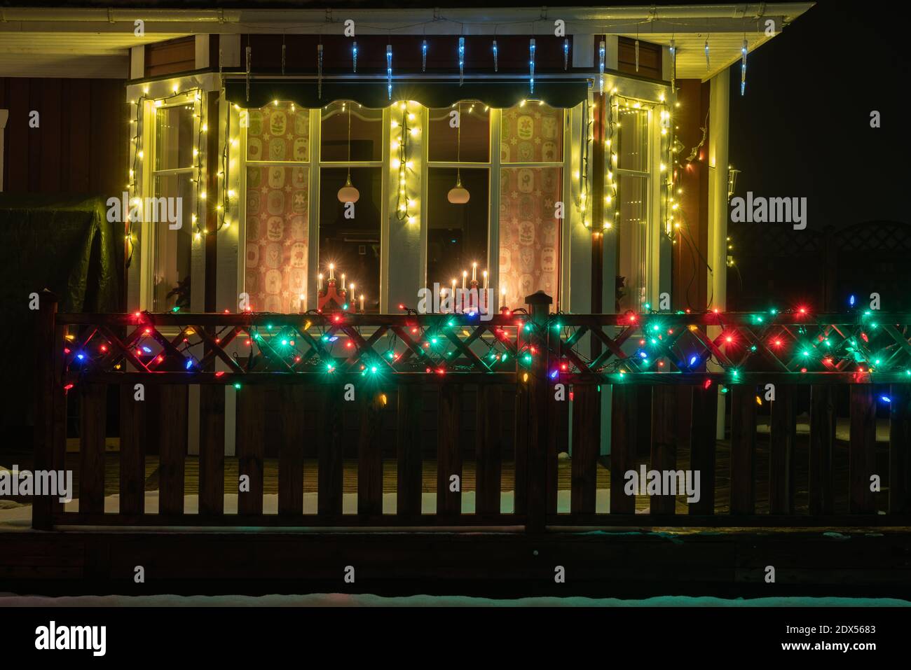 Vue rapprochée sur la maison suédoise rouge en bois avec fenêtre traditionnelle chandelier de l'avent et clôture de terrasse en bois avec éclairage multicolore pour Christma Banque D'Images