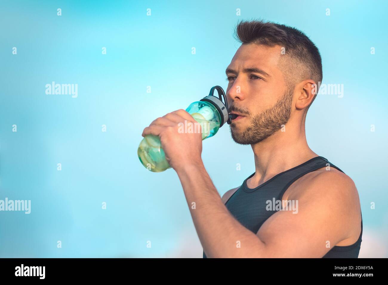 Jeune homme musculaire de forme physique boire de l'eau de citron détox de bouteille réutilisable pendant un entraînement. Boire tout en faisant de l'exercice. Banque D'Images