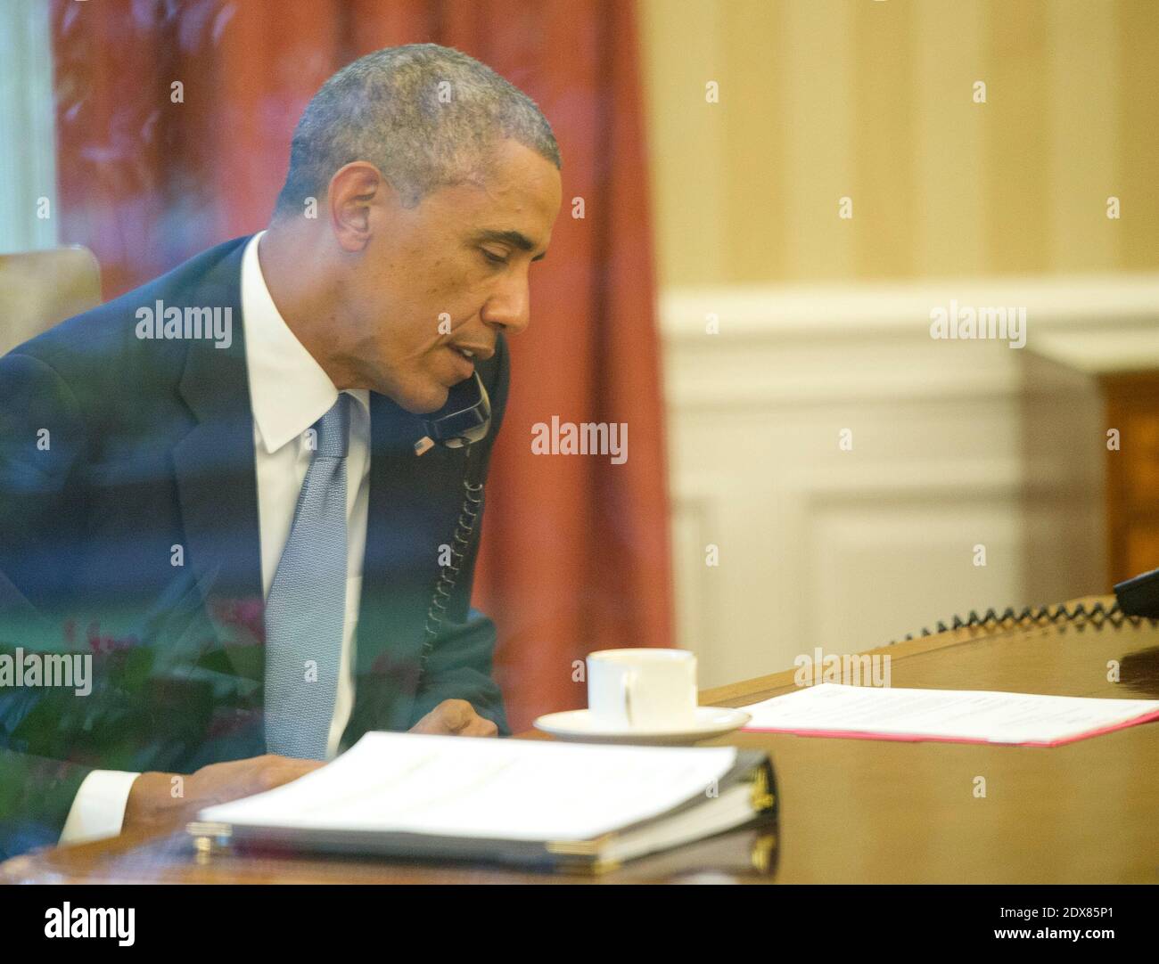 Le président des États-Unis Barack Obama est photographié à travers une fenêtre du Bureau ovale lorsqu'il parle au téléphone avec le roi Abdallah Abd al Aziz du Royaume d'Arabie Saoudite à la Maison Blanche à Washington, D.C., aux États-Unis le mercredi 10 septembre 2014, alors qu'il se prépare à son discours à la nation ce soir. Photo Pool par Ron Sachs/ABACAPRESS.COM Banque D'Images