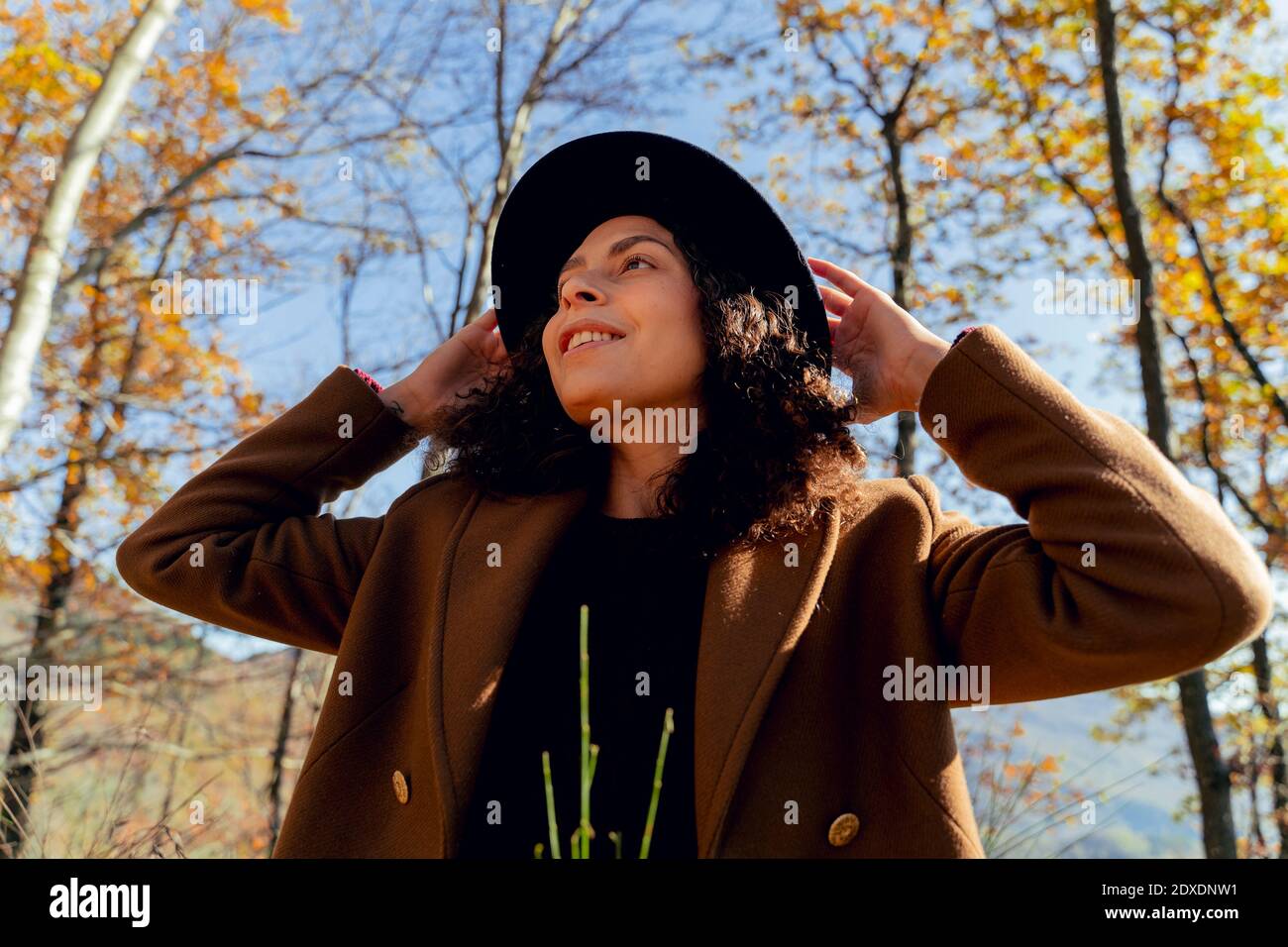 Femme souriante portant un chapeau qui regarde loin en forêt Banque D'Images
