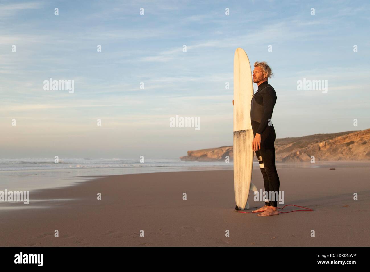 Surfeur regardant loin en se tenant à la plage contre ciel Banque D'Images
