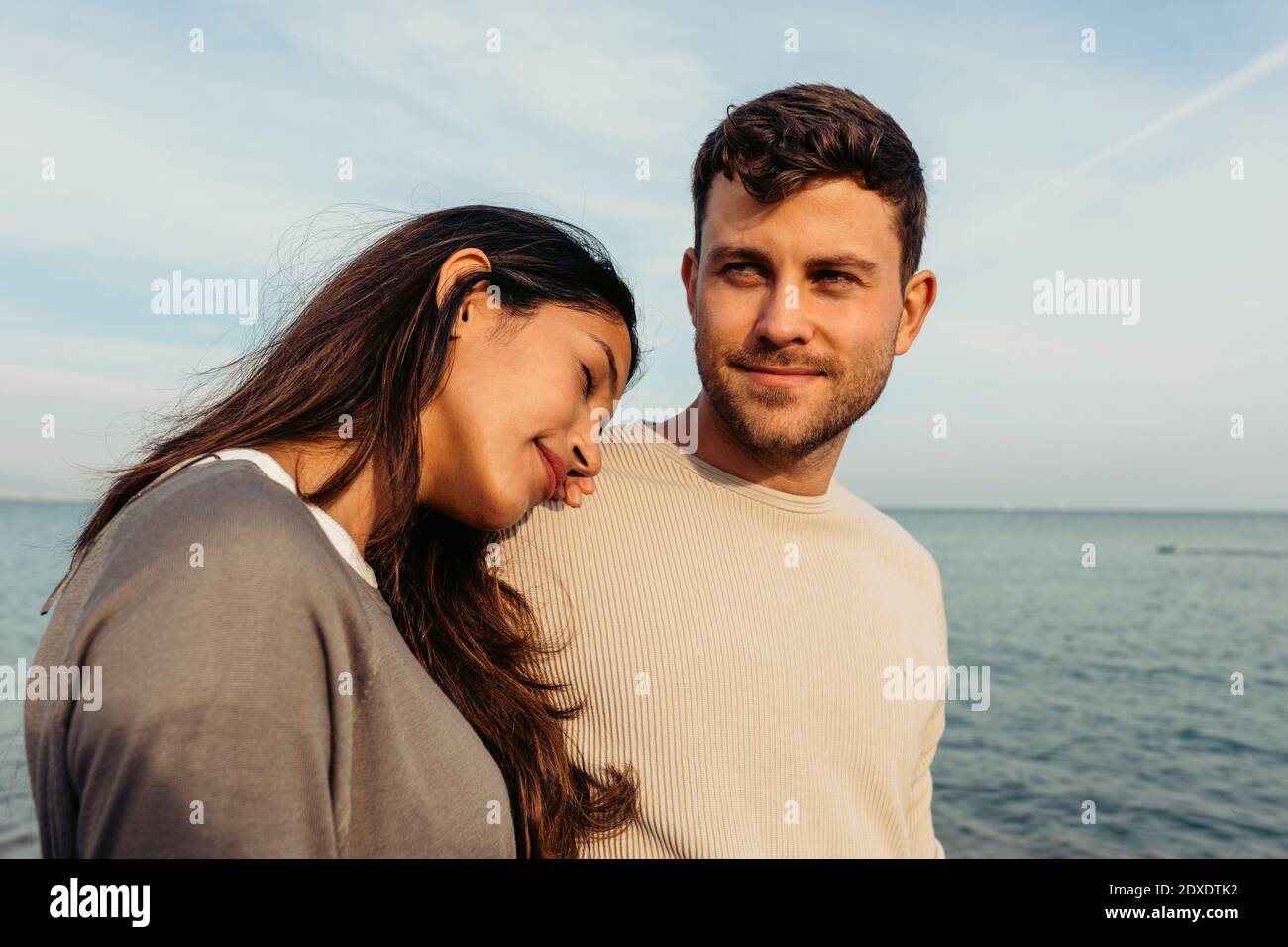 Jeune femme se penchée sur l'épaule de l'homme contre le ciel à la plage Banque D'Images