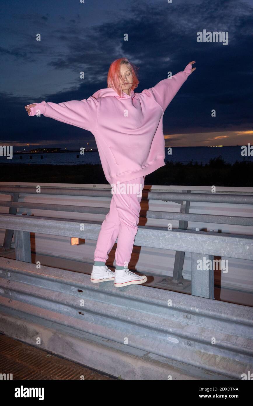 Jeune femme aux cheveux roses portant un costume d'athlétisme rose debout sur la barrière routière la nuit Banque D'Images