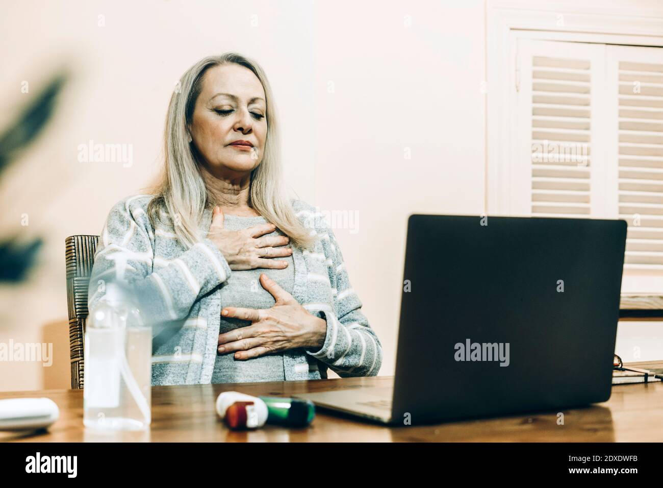 Femme âgée faisant de l'exercice de respiration pendant la consultation en ligne à la maison Banque D'Images