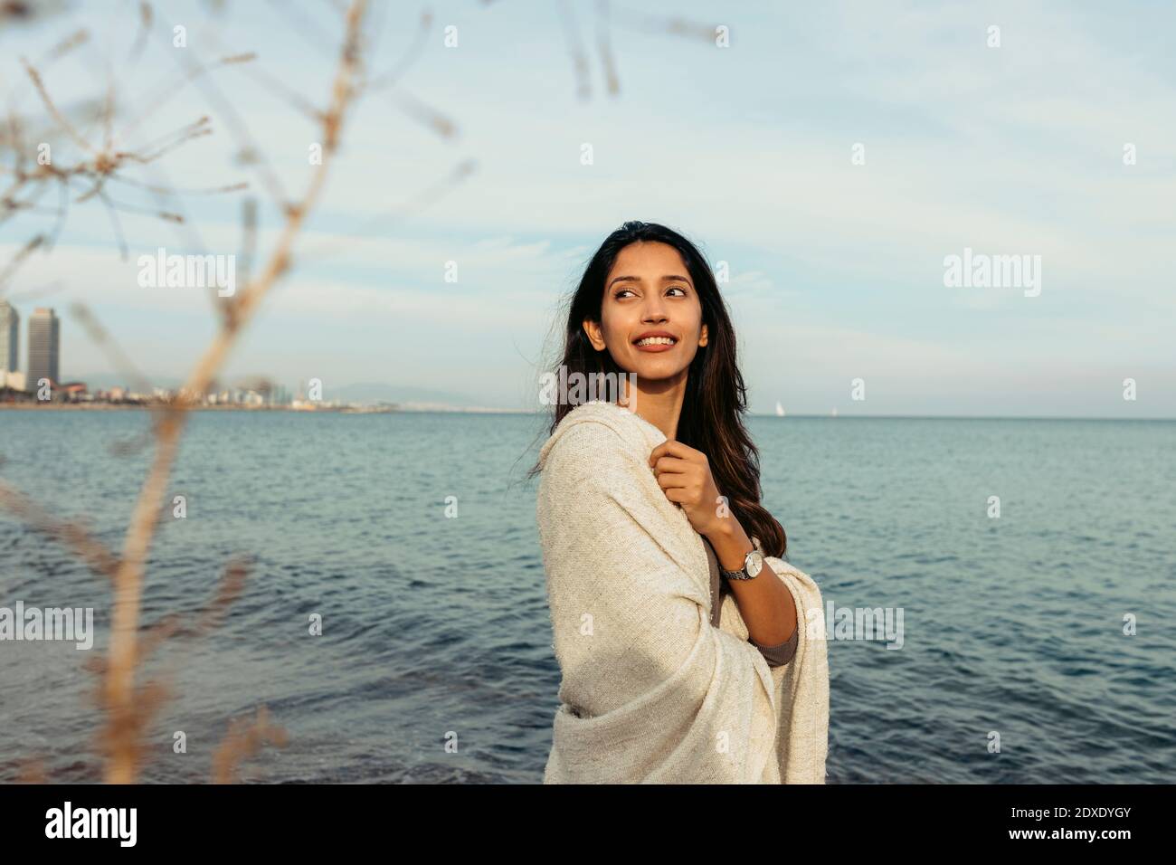 Femme souriante et attentionnée qui regarde loin tout en se tenant sur l'eau plage Banque D'Images