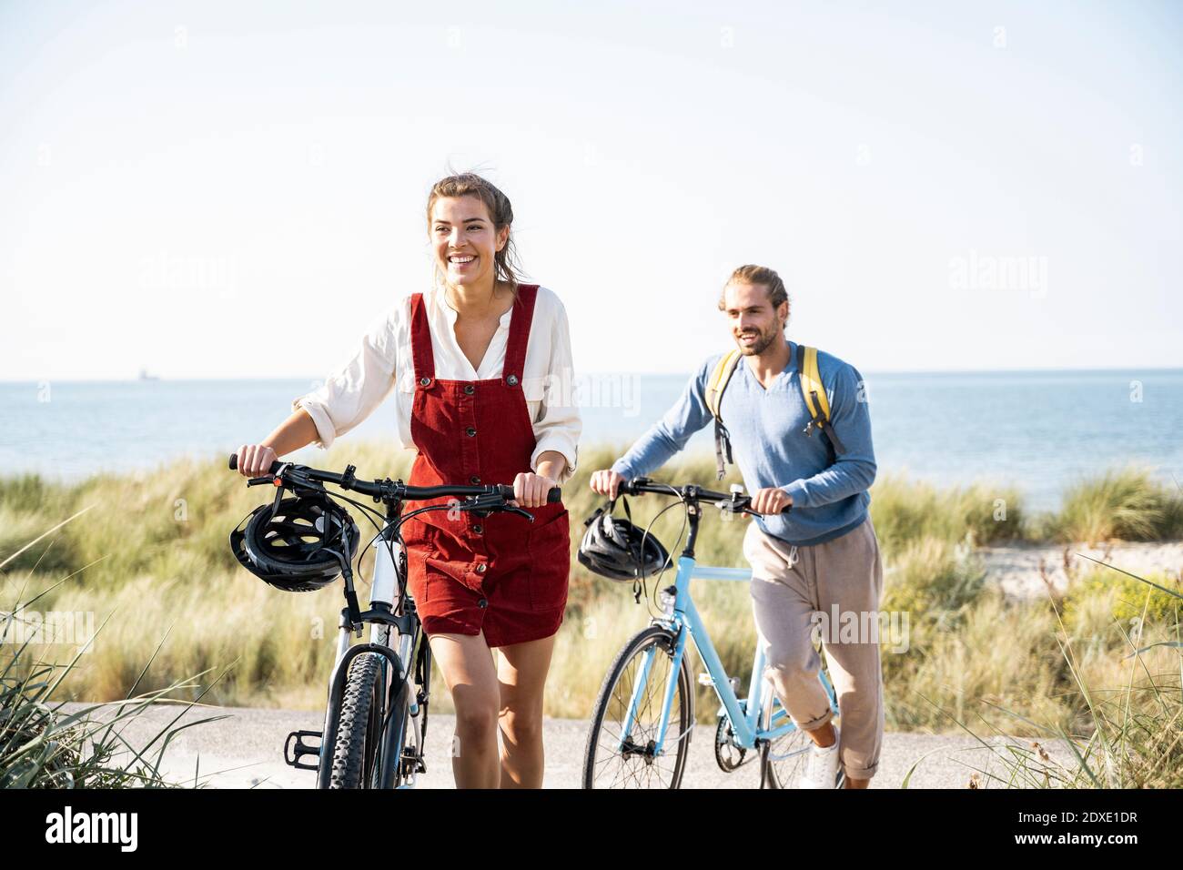 Homme souriant et femme marchant avec des vélos à la plage Banque D'Images