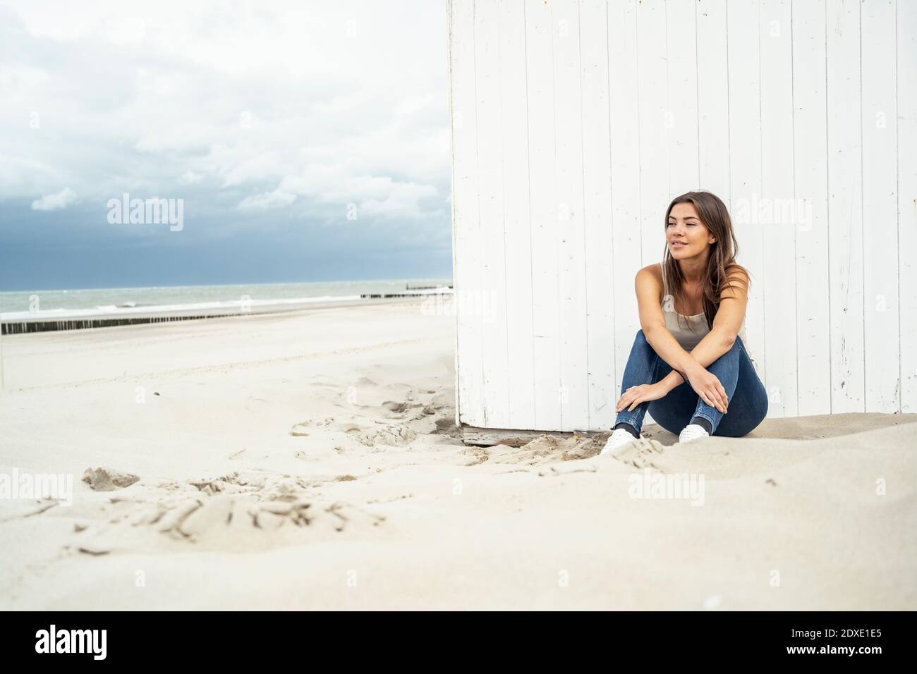 Femme souriante qui regarde loin tout en étant assise à la plage Banque D'Images