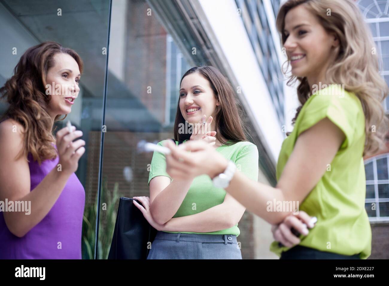 Des collègues de sexe féminin commet des potins tout en fumant des cigarettes pendant la pause à l'extérieur du bureau Banque D'Images