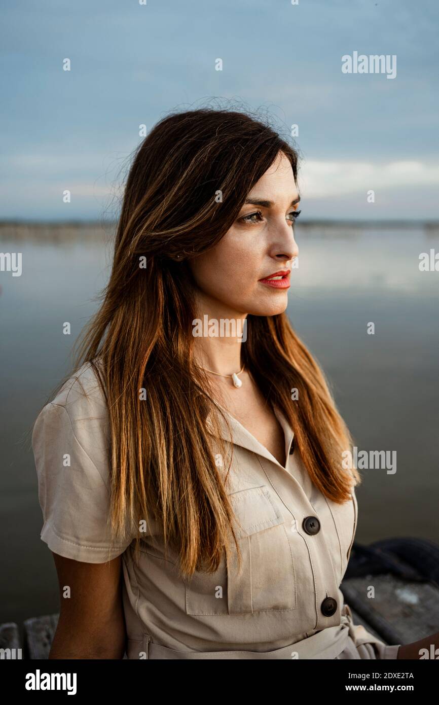 Belle femme regardant loin en s'asseyant à la jetée contre le lac Banque D'Images