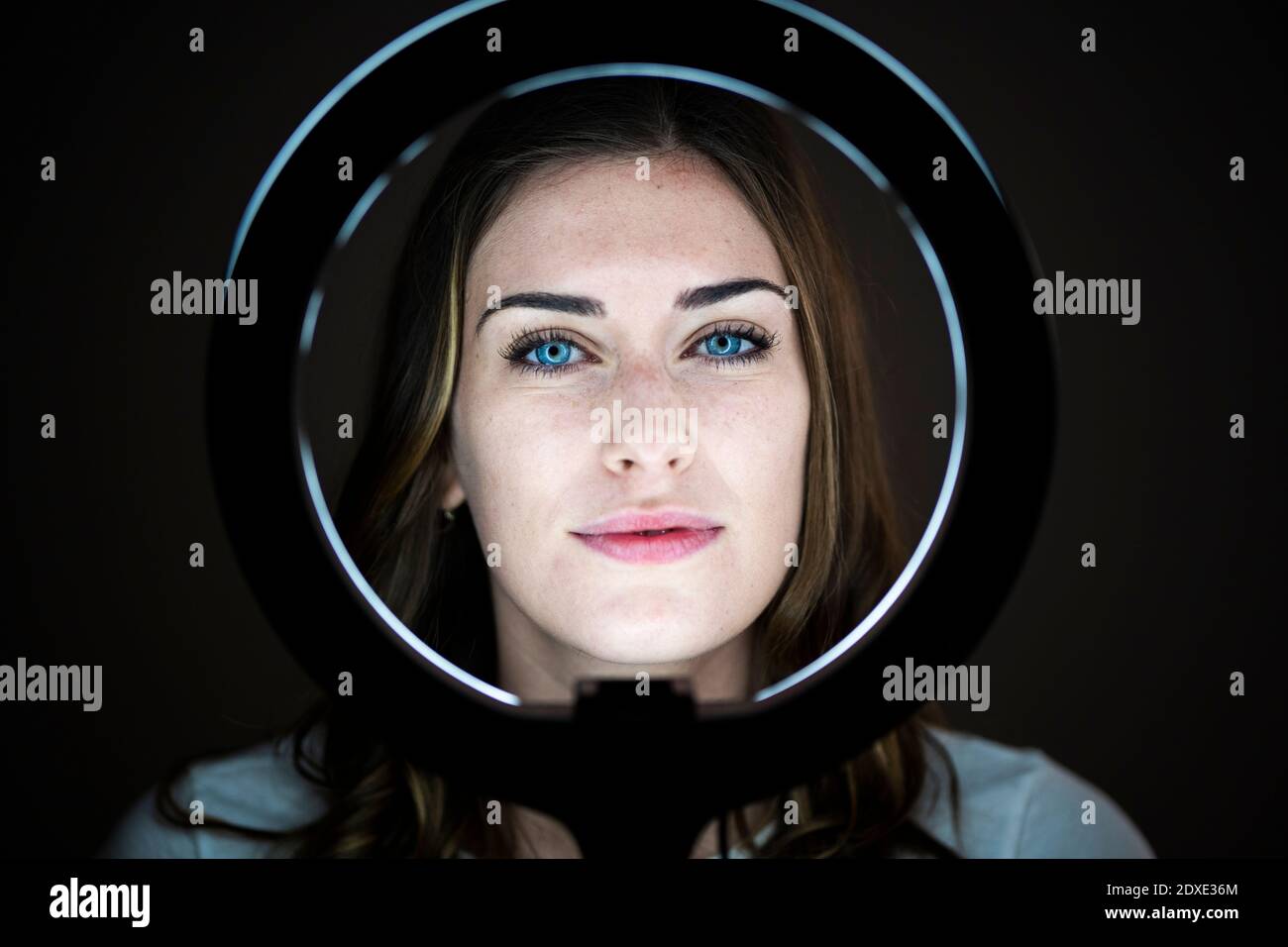 Belle jeune femme regardant à travers l'anneau lumineux dans le studio Banque D'Images