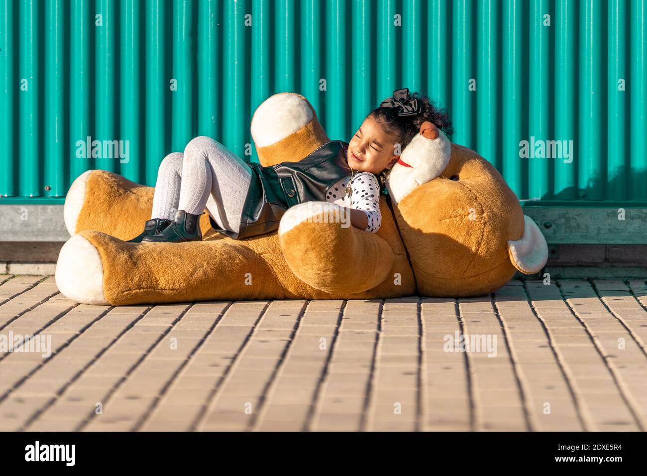 Jolie fille couchée sur un ours en peluche contre un mur vert Banque D'Images