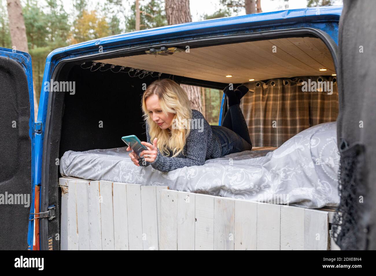 Femme adulte de taille moyenne utilisant un téléphone portable lorsqu'elle est allongée sur le lit dans le camping-auto Banque D'Images
