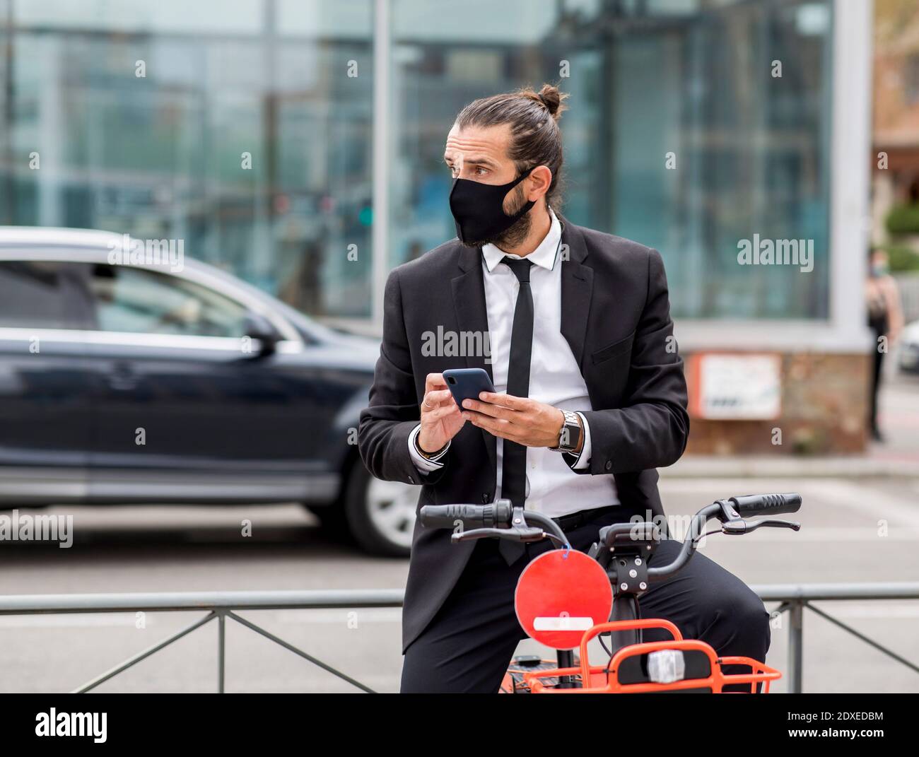 Portrait d'homme d'affaires portant un masque de protection assis sur un vélo avec un smartphone entre vos mains Banque D'Images