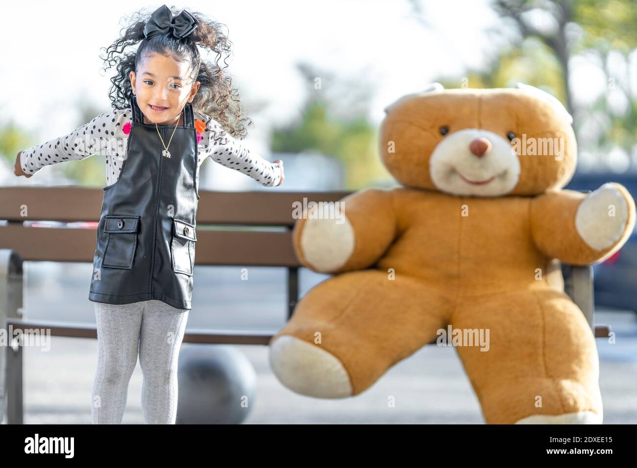 Une fille joueur sautant en jouant avec un ours en peluche sur un banc en arrière-plan Banque D'Images