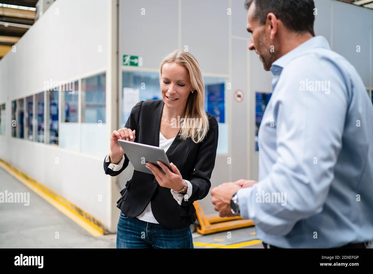 Une collègue qui utilise une tablette numérique alors qu'un homme d'affaires se tient à côté d'elle en usine Banque D'Images