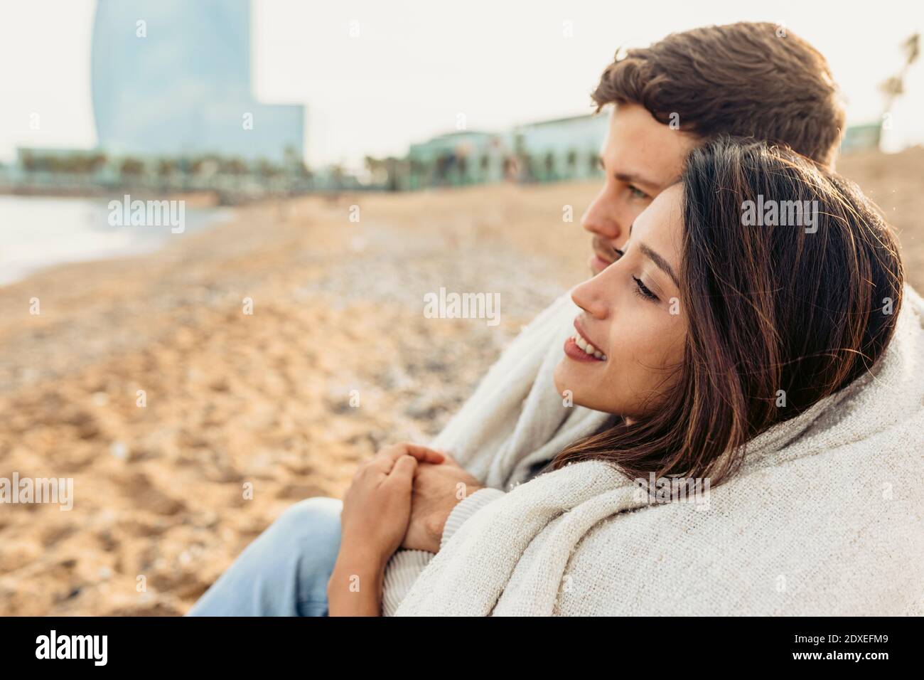 Jeune couple qui regarde loin tout en étant assis à la plage Banque D'Images
