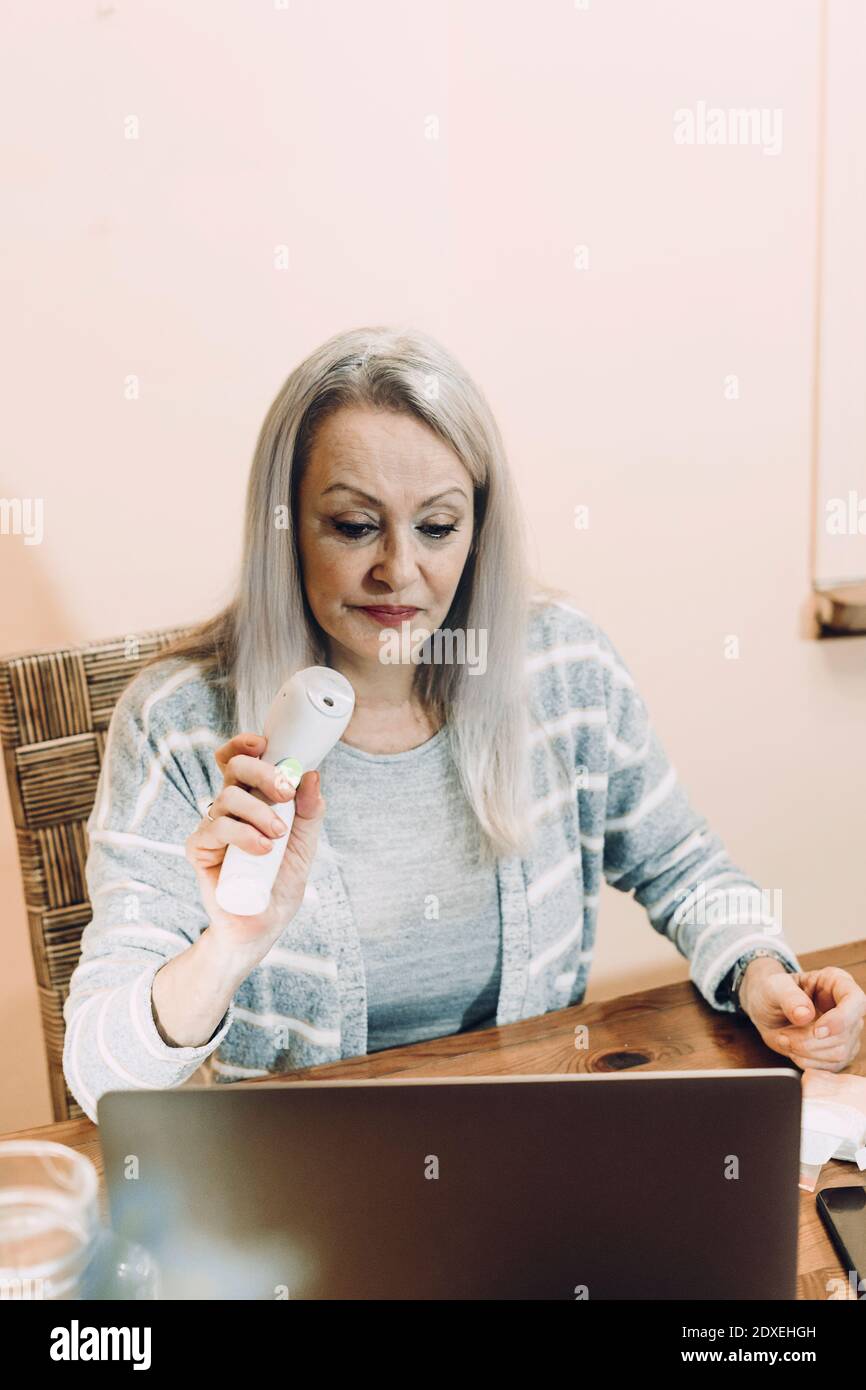 Femme âgée montrant un thermomètre infrarouge lors d'une consultation en ligne à la maison Banque D'Images