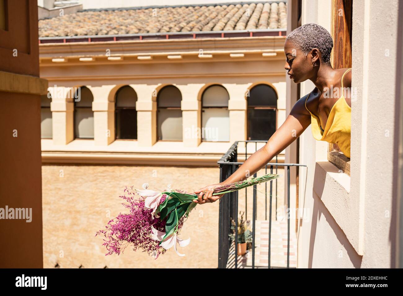 Femme à la mode tenant le bouquet de fleurs hors de la fenêtre sur ensoleillé jour Banque D'Images