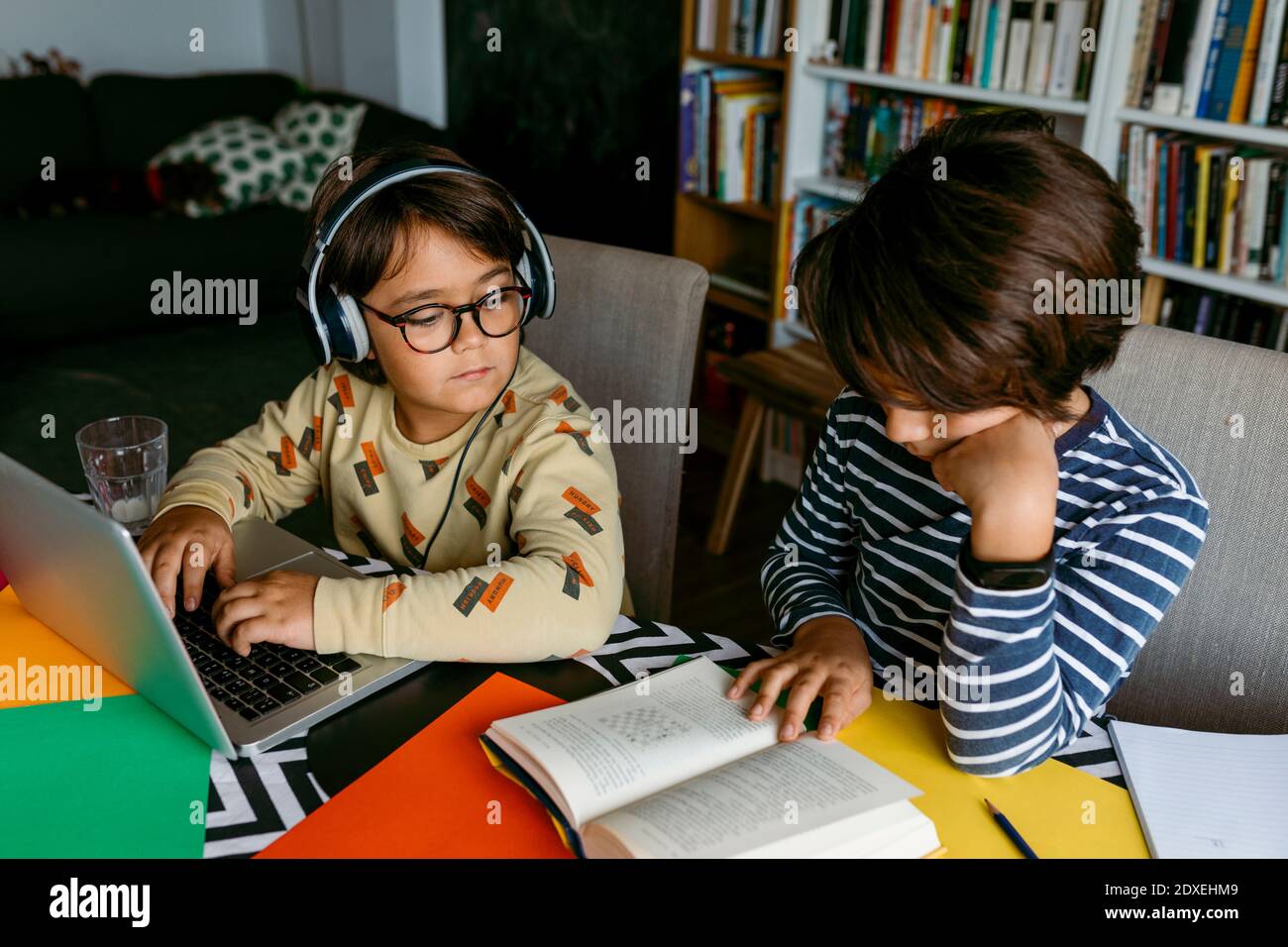 Garçon peeking alors que l'ami de sexe masculin lit le manuel à la table Banque D'Images