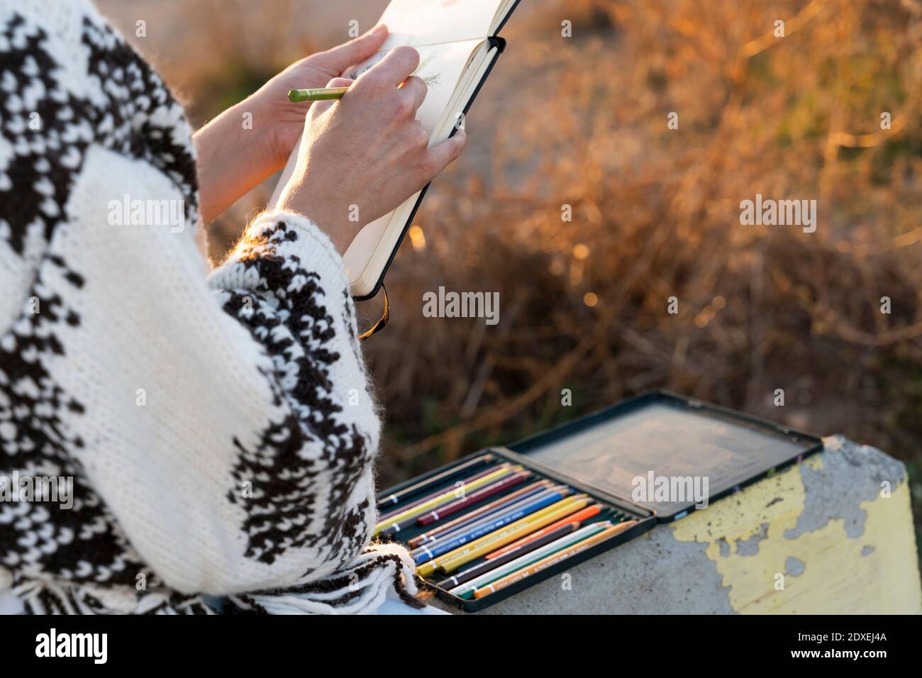 Femme qui dessine tout en étant assise sur le mur de soutènement avec des crayons de couleur Banque D'Images