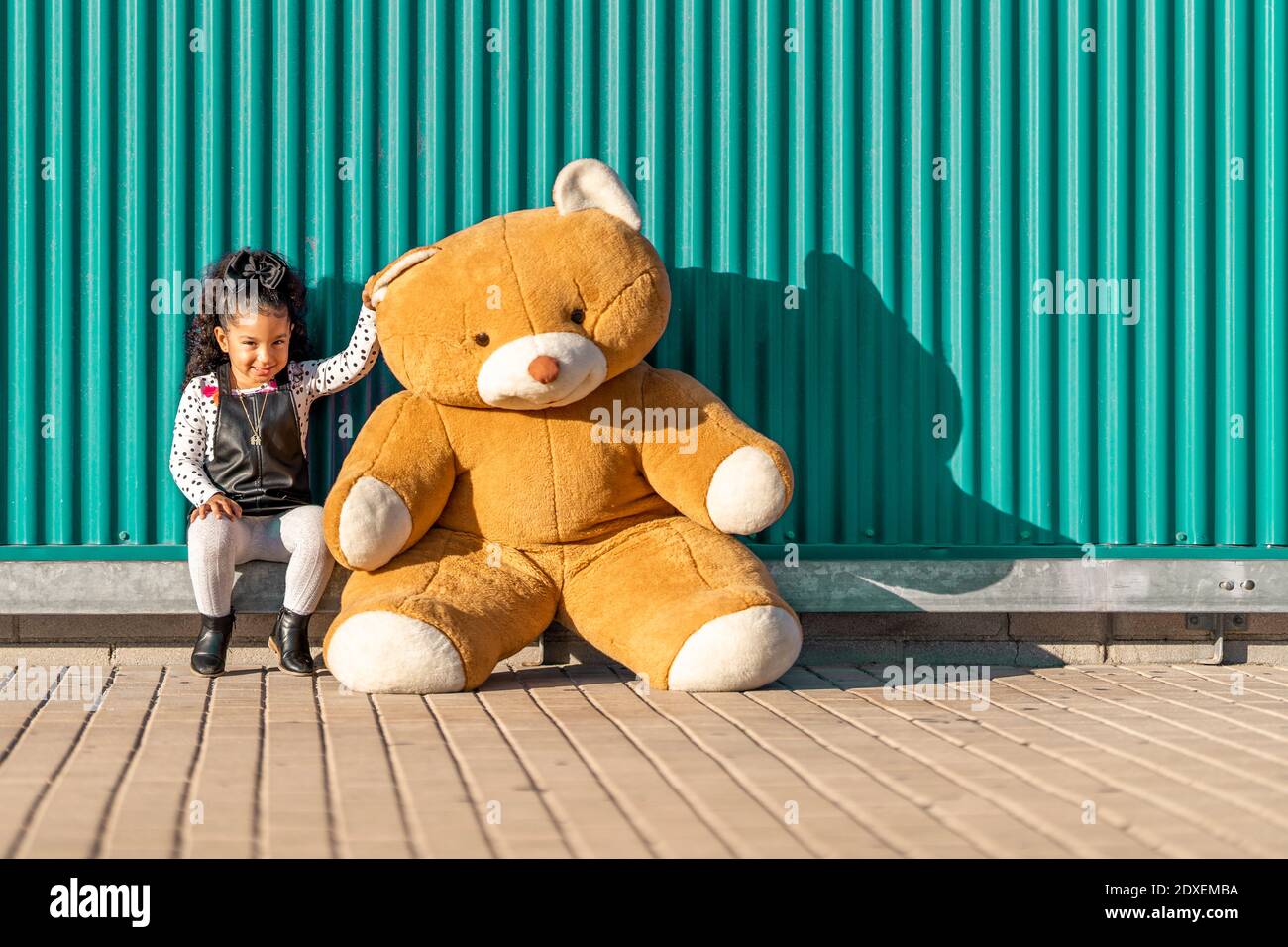 Jolie fille qui paie avec un ours en peluche tout en étant assise contre le vert mur Banque D'Images