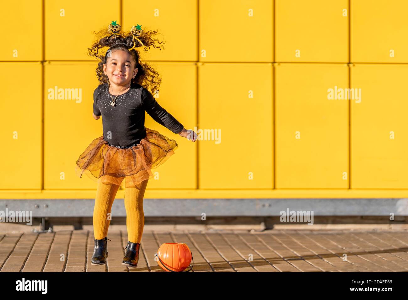 Fille avec bandeau Halloween et pot de fleur saut en jouant par rapport à la paroi à motif coché jaune Banque D'Images