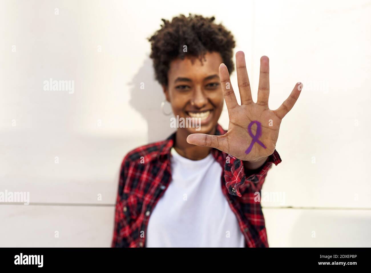 Jeune femme heureuse montrant un symbole de conscience violet sur la paume contre Mur blanc pendant la journée des femmes Banque D'Images