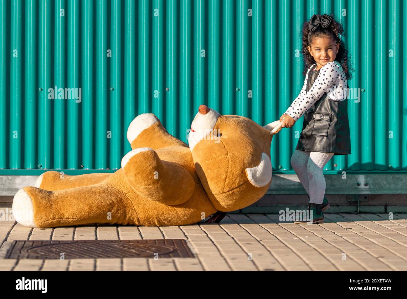 Une fille traînant un ours en peluche sur le sentier tout en se tenant contre le vert mur Banque D'Images
