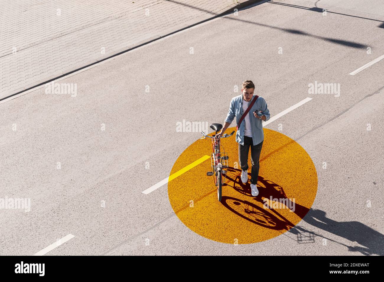 Homme avec vélo de roue en utilisant le téléphone portable tout en marchant route avec cercle doré Banque D'Images