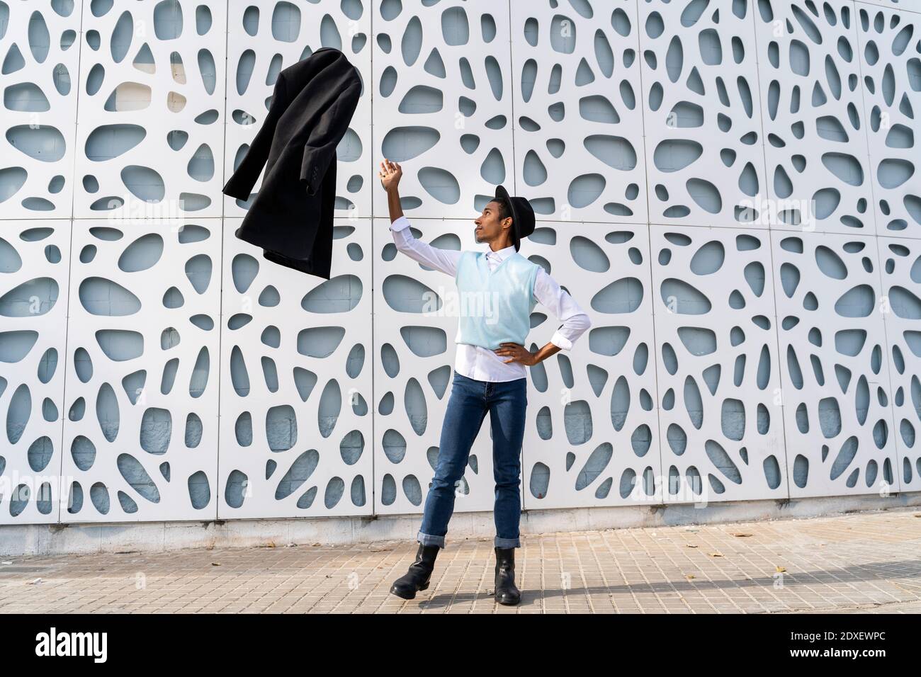 Jeune homme debout sur une jambe tout en jetant la veste air contre le mur du motif Banque D'Images
