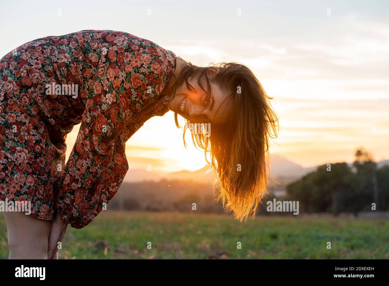 Jeune femme souriante aux cheveux bruns qui se replient au coucher du soleil Banque D'Images