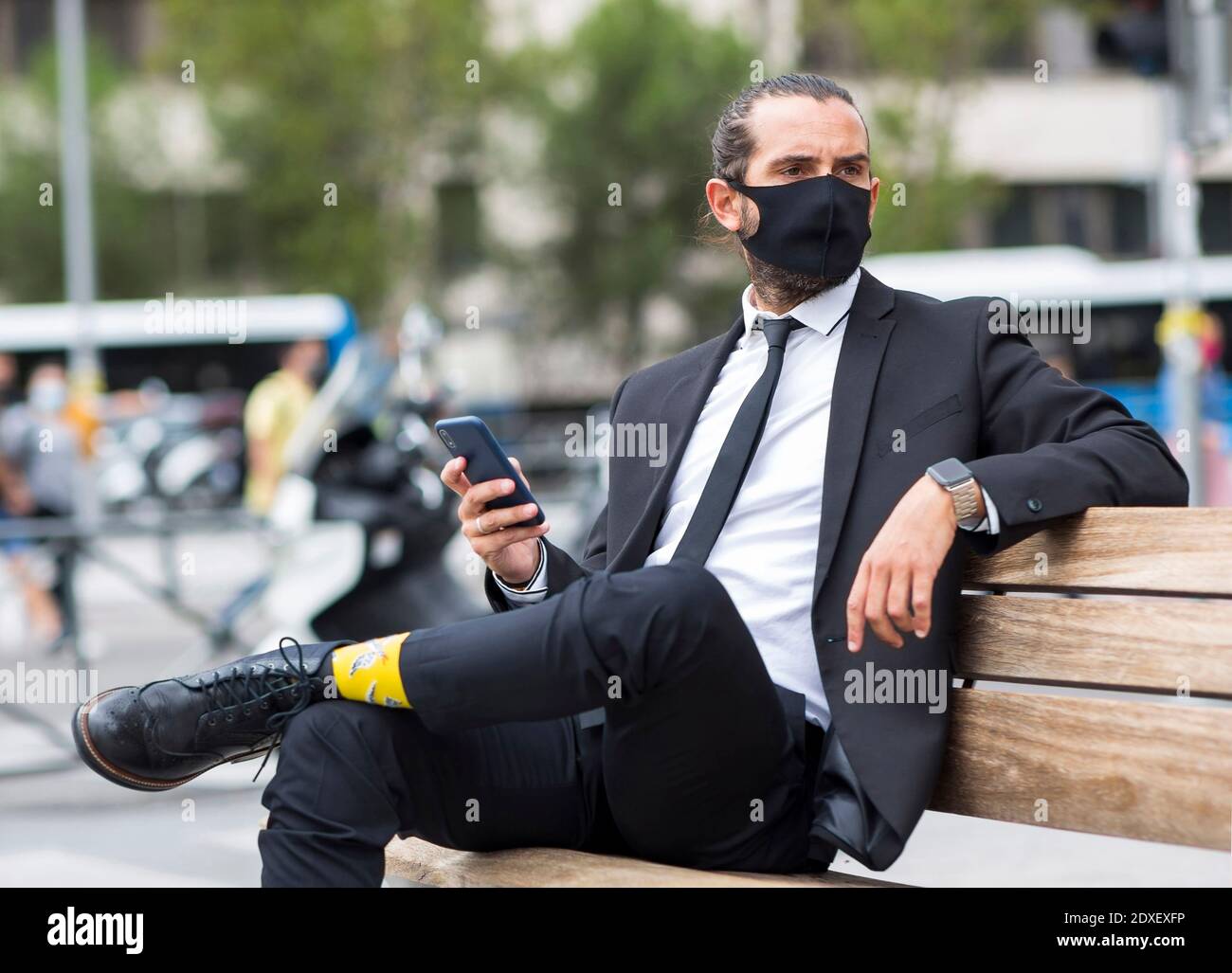 Portrait d'homme d'affaires portant un masque de protection assis sur un banc avec smartphone à portée de main Banque D'Images