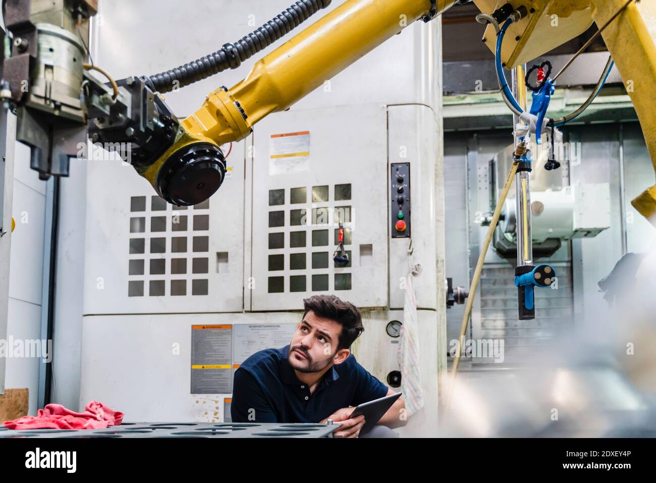 Jeune homme travailleur manuel avec tablette numérique examinant bras robotique en usine Banque D'Images