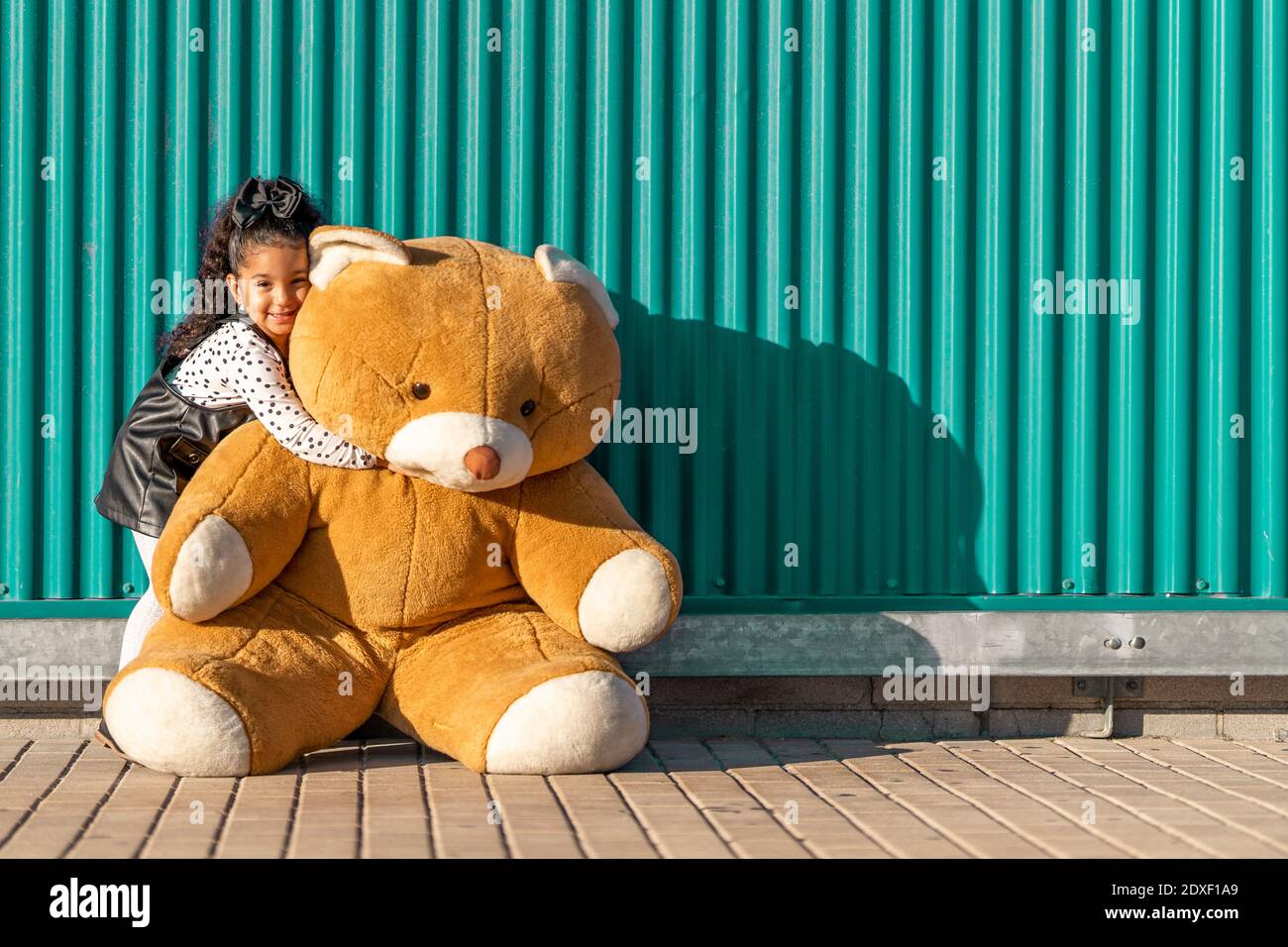 Jolie fille embrassant l'ours en peluche tout en se tenant contre le mur vert Banque D'Images