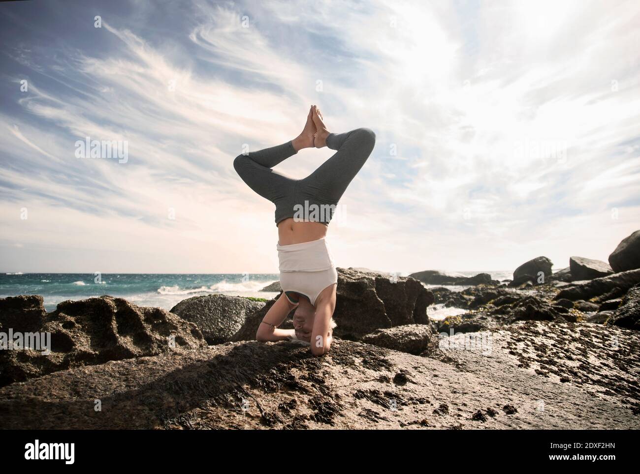 Femme pratiquant Sirsasana sur la formation de roche à la plage contre le ciel Banque D'Images