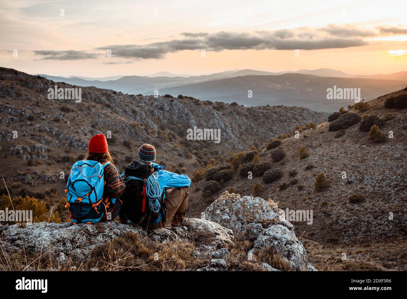 Randonneurs masculins et féminins profitant du coucher du soleil tout en étant assis sur le rocher montagne pendant les vacances Banque D'Images
