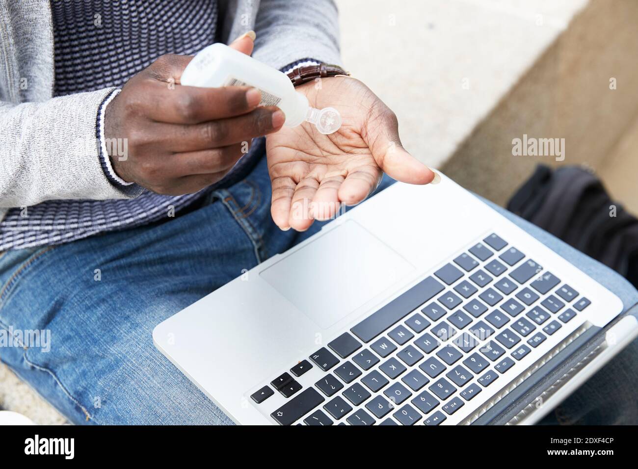 Homme d'affaires avec du désinfectant à portée de main tout en étant assis avec un ordinateur portable pendant une pandémie Banque D'Images